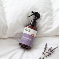 Bottle of 'Blissful Dreams' lavender spray on a white surface with lavender flowers.