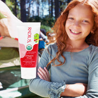 Child holding a tube of Radius Organic Toothpaste with dragon fruit flavor outdoors.