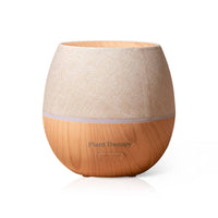 Plant Therapy essential oil diffuser with a natural wood base, a light beige textured fabric upper section, and a subtle purple LED light strip, shown on a white background.