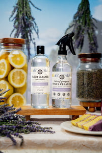 Two bottles of cleaning products on a wooden stand with lemons and lavender in the background.