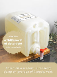 Large laundry detergent container with a pump on a wooden surface, featuring text about detergent quantity.
