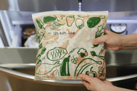 Person holding a package of 'Chicken Soup' with plant illustrations in a kitchen setting