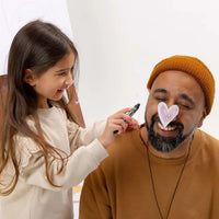 A young girl drawing on a man's face with a marker, both smiling.