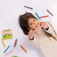 Child holding a pink crayon with colorful crayons scattered around on a white floor.
