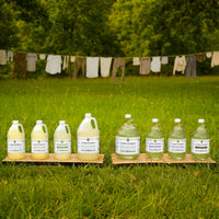 Bottles of laundry detergent on wooden stands in a grassy field with clothesline in the background