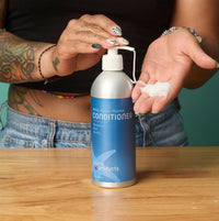 Person holding a bottle of conditioner with visible branding on a wooden surface.