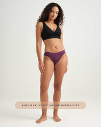 Woman wearing a black bikini top and purple bottoms on a white background