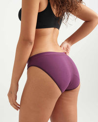 Person wearing purple bikini bottoms and black top on a light background
