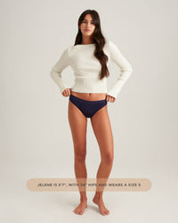 Woman wearing a white sweater and dark blue bikini bottoms on a plain background