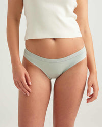 Person wearing light green bikini bottoms and a white top on a plain background