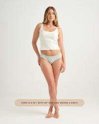 Woman wearing a white tank top and light blue underwear on a plain background