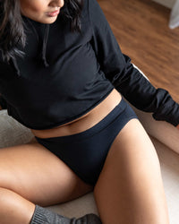 Person wearing a black outfit sitting on a wooden floor.