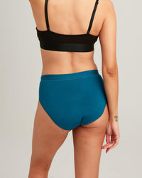 Person wearing a black bikini top and teal high-waisted bikini bottom on a light gray background