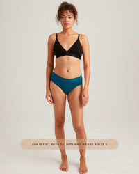 Woman wearing a black bikini top and teal high-waisted bikini bottom on a light gray background.