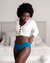 Woman wearing a white cardigan and blue underwear in a bedroom setting
