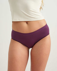 A close-up of a model wearing a pair of solid purple high-waisted briefs, paired with a white cropped tank top, against a light gray studio background.