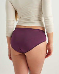 Person wearing a beige long-sleeve top and purple high-waisted underwear on a white background