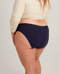 Person wearing navy high-waisted bikini bottoms with a plain background