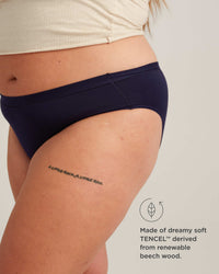 Person wearing navy blue underwear with a tattoo on their leg, on a plain background.