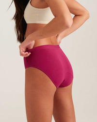Person wearing a white sports bra and pink high-waisted underwear on a plain background