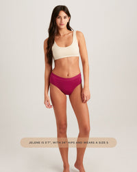 Woman wearing a beige sports bra and pink high-waisted bikini bottoms on a light gray background.
