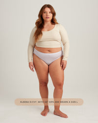 Woman wearing a beige long-sleeve top and light gray underwear on a white background