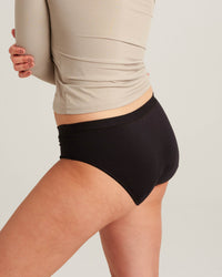 Person wearing black underwear and a beige top on a plain background