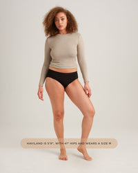 Woman wearing a beige long-sleeve top and black underwear on a white background