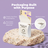 A box of Radius Silk Floss displayed on a textured stone prop against a lavender background, with marketing text and callouts about plastic-free packaging, recycled eco-carton dispenser, and a built-in cutter.
