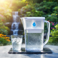 Clear water pitcher with glass of water outdoors near a waterfall
