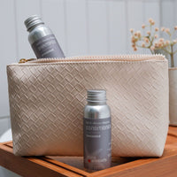 Unscented shampoo and conditioner bottles with a beige woven pouch on a wooden surface.