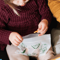 Child holding a snack bag with green illustrations of fruits and vegetables.