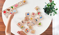 A top-down view of a child's hands interacting with a set of wooden alphabet and basic learning blocks arranged on a white round table next to a potted plant.
