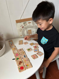 Child playing with wooden cards at a table against a white wall.