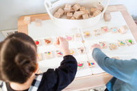 Two children playing with wooden blocks and cards on a table.