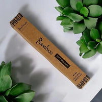 Bamboo toothbrush packaging on a white surface with green plants