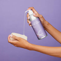 Person holding a purple bottle of body wash and a white sponge against a purple background