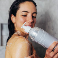 Woman applying body wash to her shoulder with a bottle labeled 'Body Wash'.