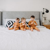 Three children in matching outfits sitting on a bed in a bedroom setting.