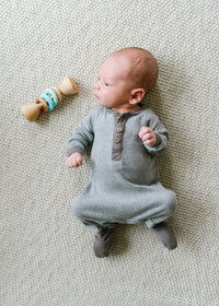 Baby in a gray onesie lying on a textured surface with a wooden toy nearby
