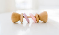 Wooden baby rattle with pink accents on a white background