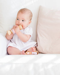Baby in a white outfit sitting on a white couch with a wooden toy.
