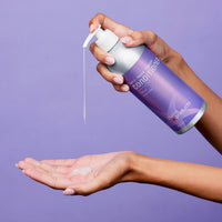 Hand holding a purple can of plant-based conditioner with a visible label against a purple background