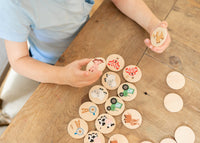 Child playing with wooden discs featuring animal illustrations on a wooden table.