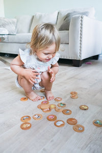 Child playing with decorative cookies on a light wood floor.