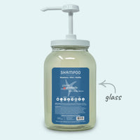 Glass shampoo bottle with pump and blue label on a light gray background